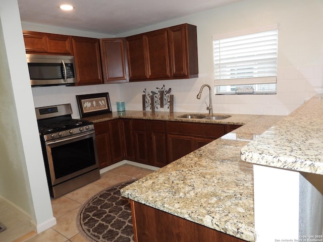 kitchen featuring appliances with stainless steel finishes, sink, light tile patterned floors, light stone counters, and kitchen peninsula