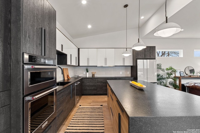 kitchen featuring white cabinets, backsplash, hanging light fixtures, white fridge, and stainless steel double oven