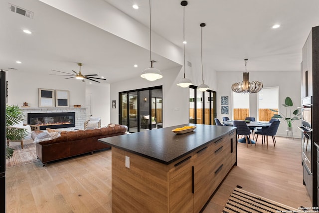 kitchen featuring pendant lighting, a stone fireplace, light hardwood / wood-style floors, and a kitchen island