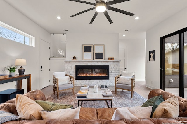 living room with a fireplace, ceiling fan, and light wood-type flooring