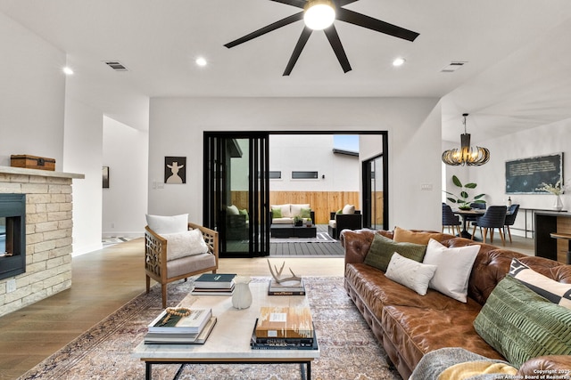 living room with hardwood / wood-style flooring, a fireplace, and ceiling fan with notable chandelier