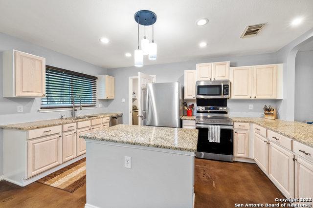 kitchen featuring sink, hanging light fixtures, a center island, light stone counters, and stainless steel appliances