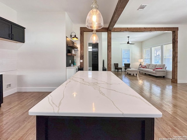 kitchen with light stone counters, decorative light fixtures, light hardwood / wood-style flooring, and beamed ceiling