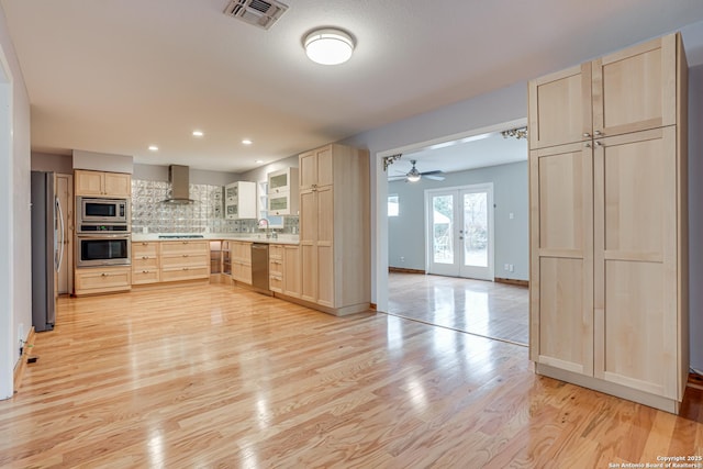 kitchen featuring appliances with stainless steel finishes, wall chimney exhaust hood, light brown cabinetry, and decorative backsplash