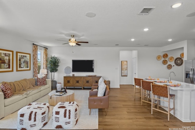 living room featuring ceiling fan, a textured ceiling, and light wood-type flooring