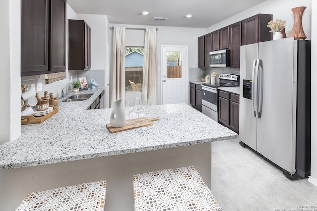 kitchen with sink, stainless steel appliances, tasteful backsplash, light stone countertops, and kitchen peninsula