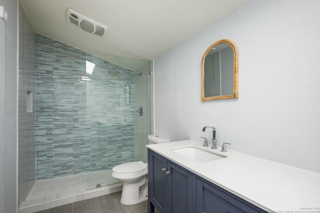 bathroom with vanity, lofted ceiling, toilet, and a tile shower