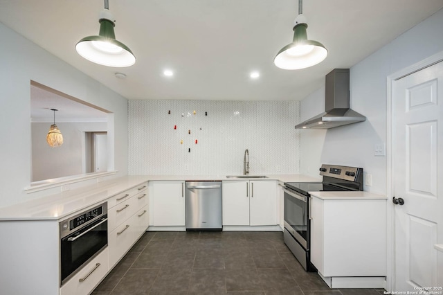 kitchen featuring pendant lighting, wall chimney range hood, sink, white cabinetry, and stainless steel appliances