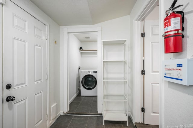 clothes washing area with washer / clothes dryer, a textured ceiling, and dark tile patterned flooring