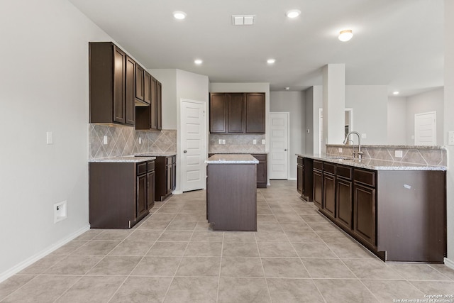 kitchen featuring visible vents, decorative backsplash, a center island, dark brown cabinets, and a sink