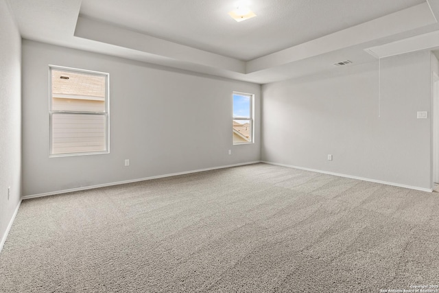 spare room with visible vents, a tray ceiling, carpet, and attic access