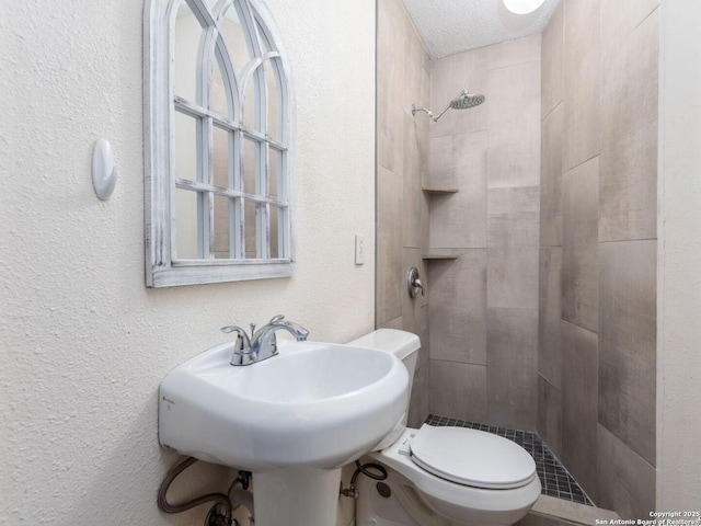 bathroom featuring toilet, sink, a textured ceiling, and a tile shower