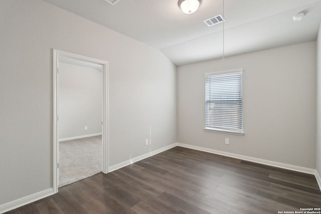 spare room with vaulted ceiling, dark wood-style floors, visible vents, and baseboards