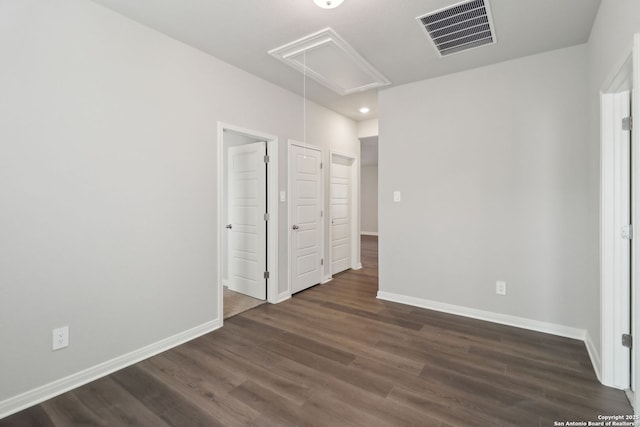 unfurnished bedroom featuring visible vents, baseboards, attic access, and wood finished floors