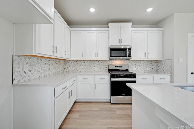 kitchen featuring white cabinets, stainless steel appliances, light wood finished floors, and backsplash