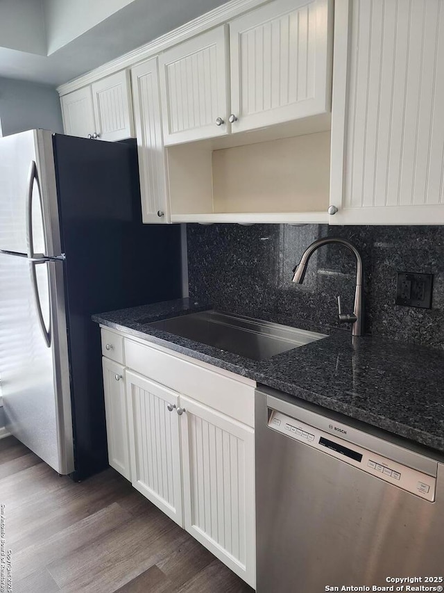 kitchen featuring dark wood-type flooring, sink, dark stone counters, stainless steel appliances, and white cabinets