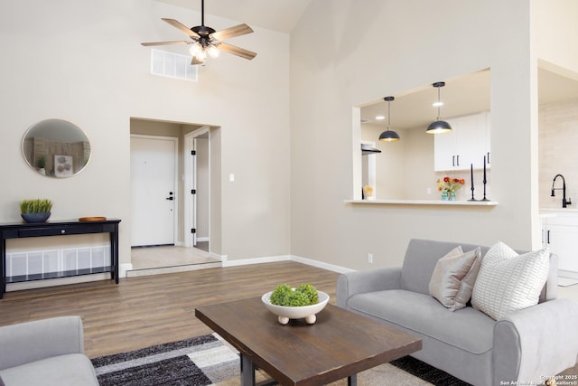 living room with hardwood / wood-style flooring, ceiling fan, sink, and a high ceiling