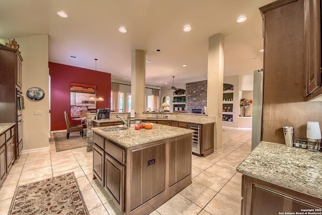 kitchen featuring built in features, sink, a kitchen island with sink, light tile patterned floors, and light stone counters