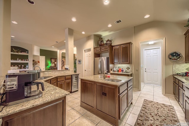 kitchen with sink, decorative backsplash, stainless steel fridge, and an island with sink