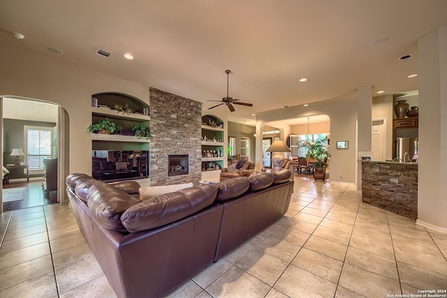 living room featuring built in shelves, ceiling fan, a stone fireplace, and light tile patterned flooring