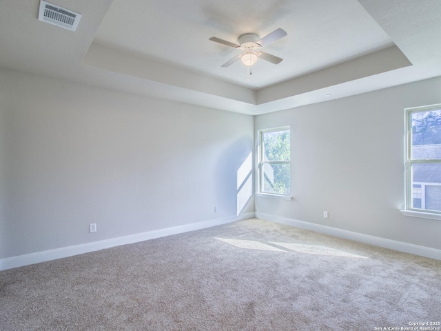 spare room with ceiling fan, a tray ceiling, and light carpet