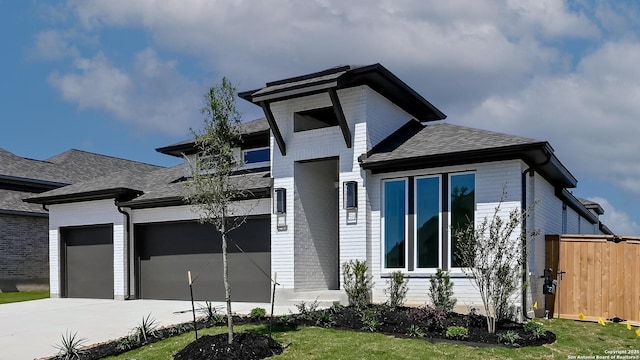 prairie-style home with an attached garage, roof with shingles, fence, and concrete driveway