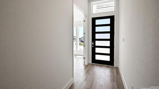 doorway to outside with baseboards, a textured wall, and wood finished floors