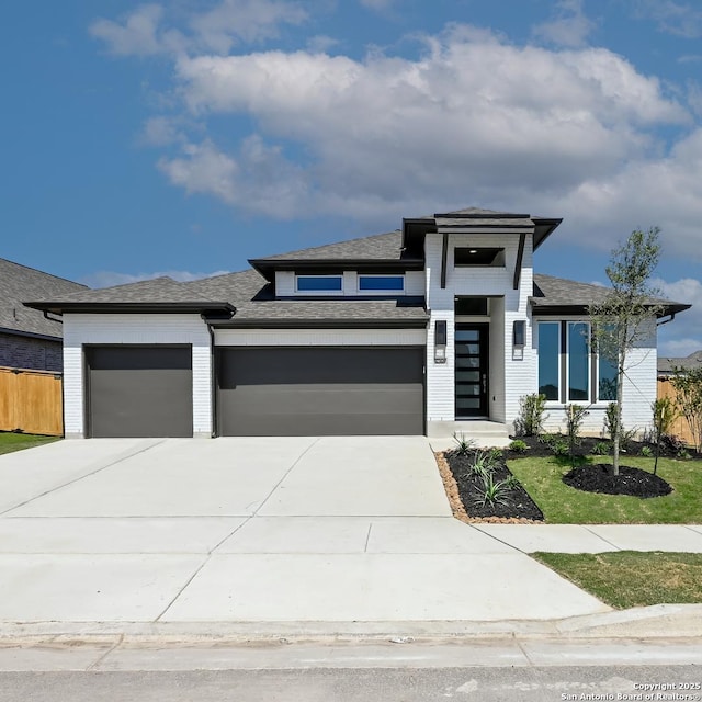 prairie-style house with an attached garage, roof with shingles, fence, and driveway