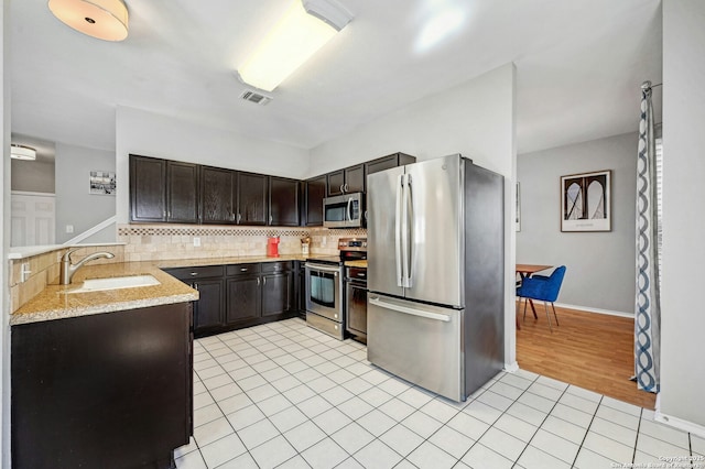 kitchen featuring dark brown cabinetry, tasteful backsplash, stainless steel appliances, a sink, and light tile patterned flooring