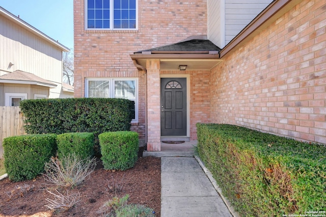 view of exterior entry featuring brick siding and fence