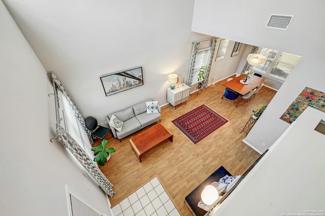 living area with baseboards, visible vents, a high ceiling, and wood finished floors