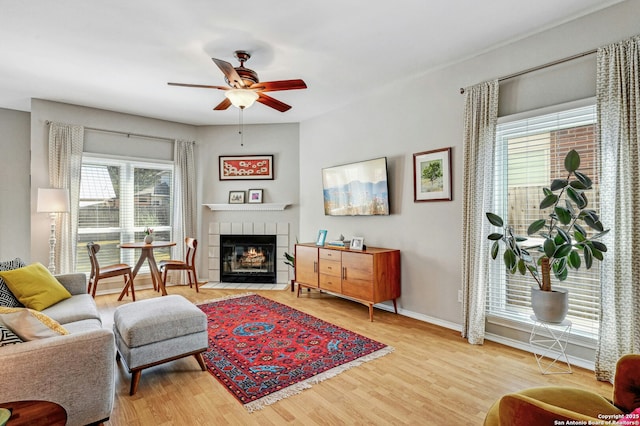 living room featuring baseboards, a fireplace, a ceiling fan, and wood finished floors