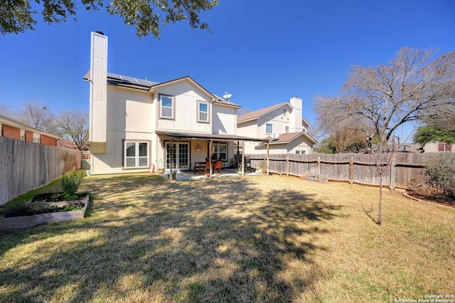 back of property with a patio, a chimney, a lawn, roof mounted solar panels, and a fenced backyard