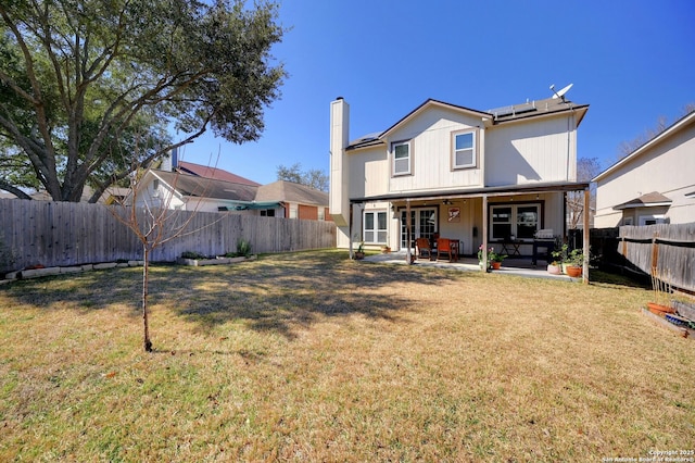 back of property with a yard, roof mounted solar panels, a fenced backyard, and a patio