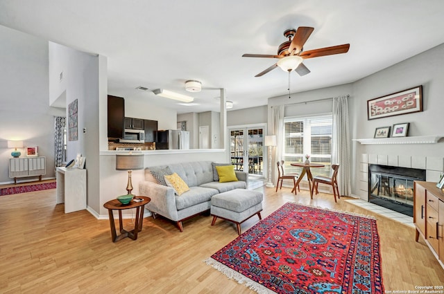 living room with a fireplace, radiator, a ceiling fan, light wood-type flooring, and baseboards