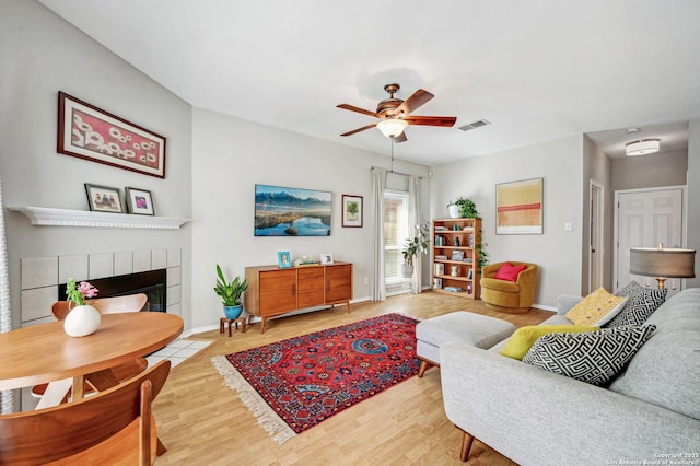 living area with light wood finished floors, baseboards, visible vents, a ceiling fan, and a fireplace