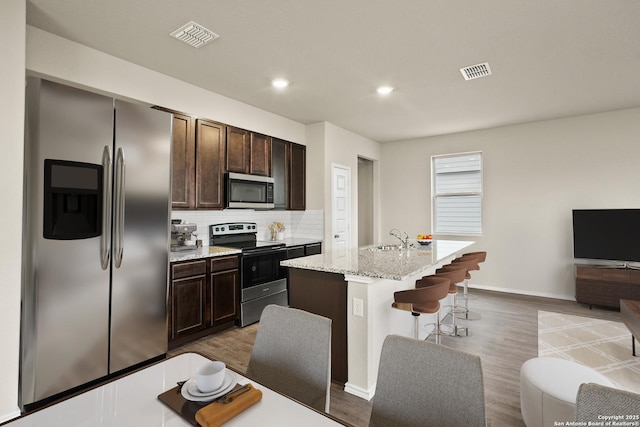 kitchen featuring dark brown cabinetry, appliances with stainless steel finishes, a breakfast bar, and a center island with sink