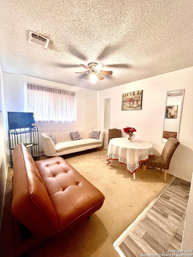 carpeted living room with ceiling fan and a textured ceiling