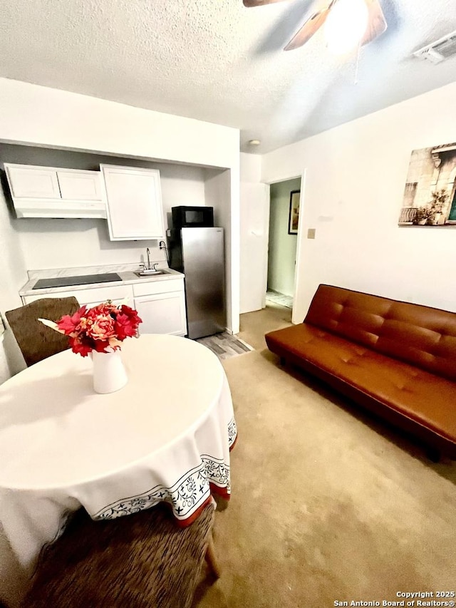 interior space with stainless steel refrigerator, white cabinets, ceiling fan, light carpet, and a textured ceiling