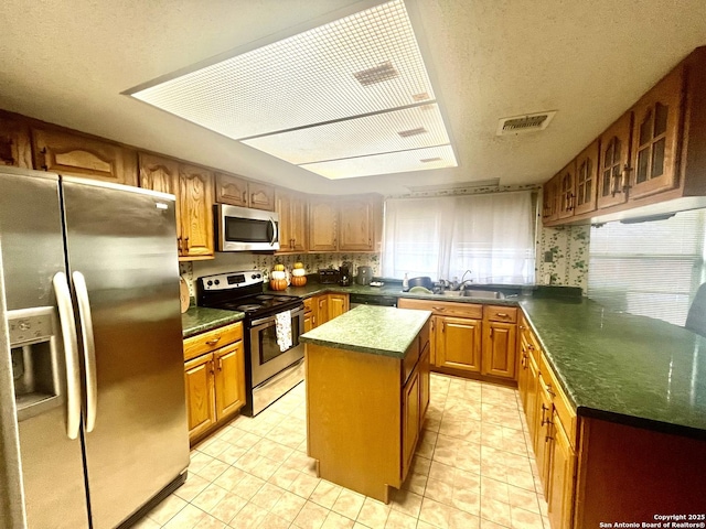 kitchen featuring a kitchen island, sink, light tile patterned floors, stainless steel appliances, and a textured ceiling