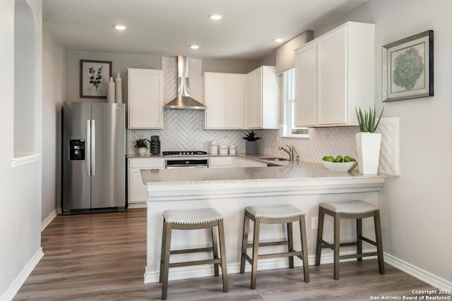 kitchen with sink, white cabinets, stainless steel fridge, light stone counters, and wall chimney exhaust hood