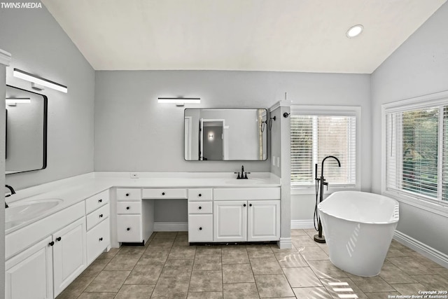 bathroom with tile patterned flooring, vaulted ceiling, a washtub, and vanity