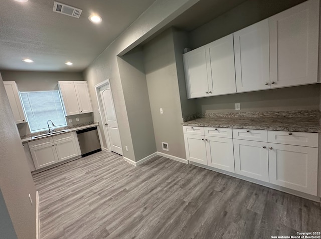 kitchen with stainless steel dishwasher, light hardwood / wood-style floors, and white cabinets