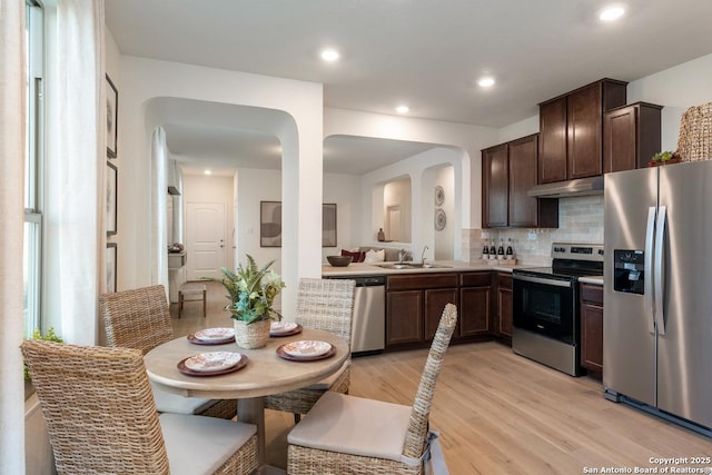 kitchen with dark brown cabinetry, sink, stainless steel appliances, light hardwood / wood-style floors, and decorative backsplash