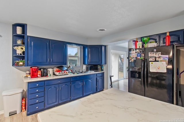 kitchen with light stone counters, sink, black refrigerator with ice dispenser, and blue cabinets