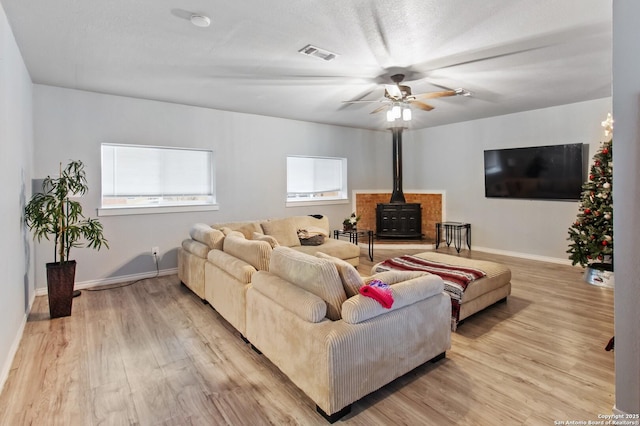 living room featuring ceiling fan, plenty of natural light, light wood-type flooring, and a wood stove