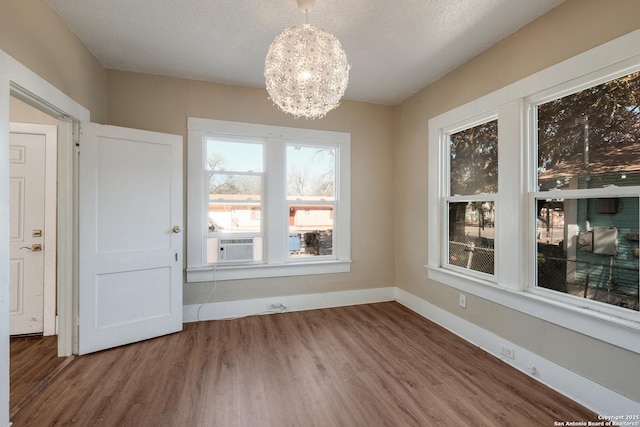 unfurnished dining area featuring an inviting chandelier, wood-type flooring, and a textured ceiling