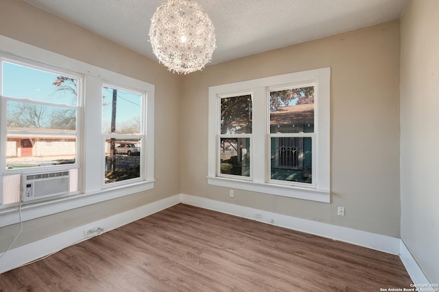 unfurnished dining area with cooling unit, a textured ceiling, wood-type flooring, and a chandelier