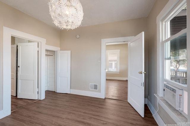 unfurnished bedroom with dark hardwood / wood-style floors, cooling unit, and a notable chandelier