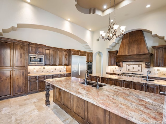 kitchen with pendant lighting, sink, premium range hood, a high ceiling, and built in appliances